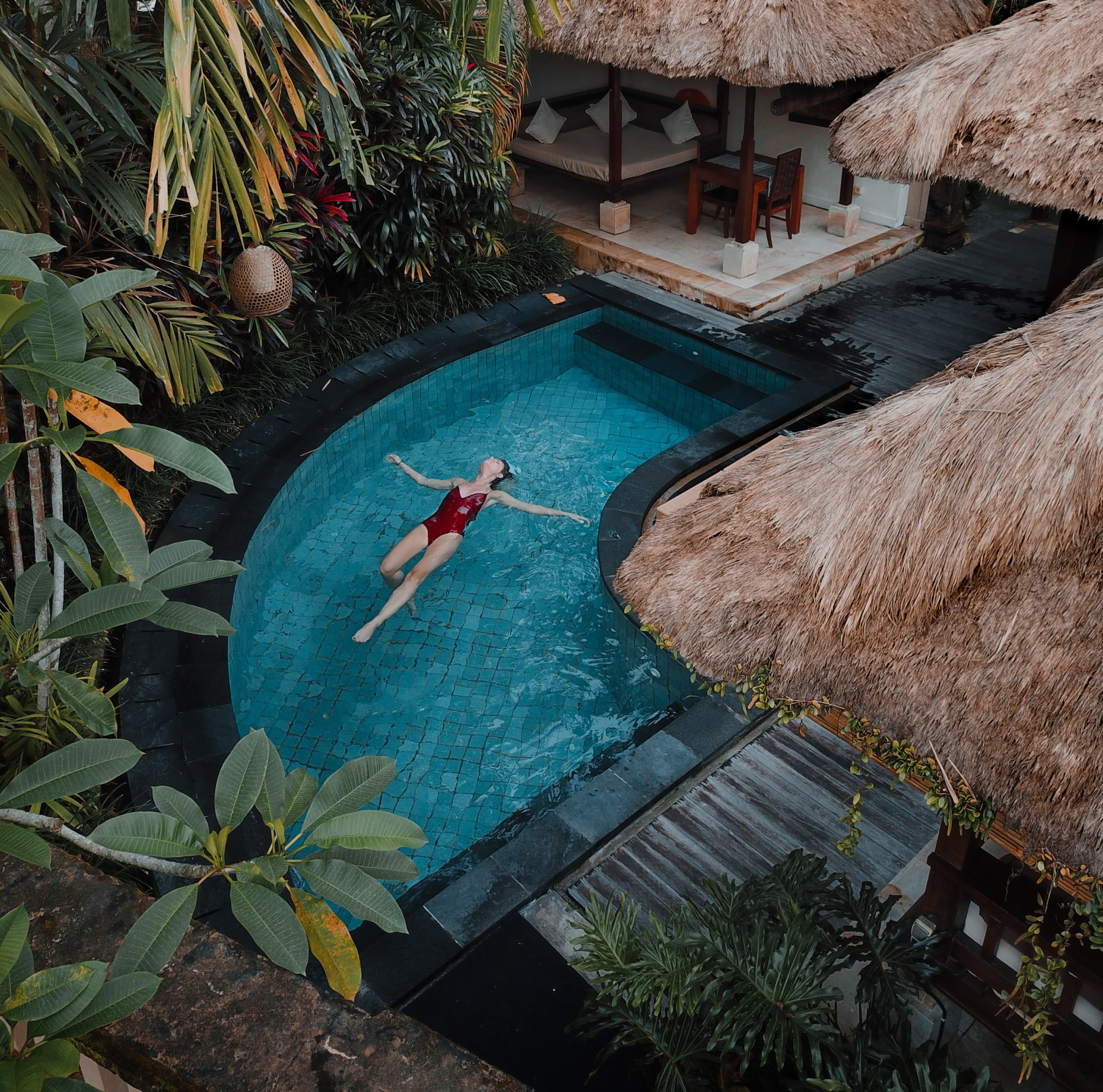 copywriting staff seo hospitality digital marketing agency female with long brown and curly hair is swimming backstroke in a villa pool in bali wearing a red one piece swimsuit